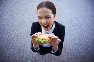 Image of very hungry businesswoman with sandwich looking at camera outside